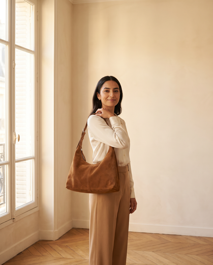 Woman in a sunlit Paris apartment carrying a caramel suede Aubrine hobo bag